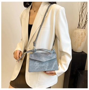Detail view of a gray-blue envelope crossbody bag with a unique knotted thin shoulder strap