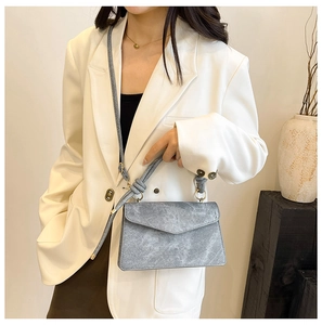 Close-up of a grey suede crossbody bag with a knotted handle and golden ring hardware