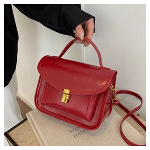 Close-up of a red glossy leather handbag with gold metal clasp and top handle