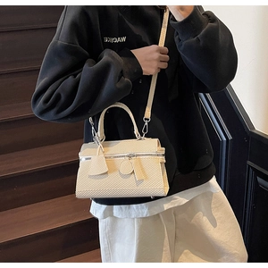 Detail of beige woven texture handbag with silver zipper and top handle on stairs