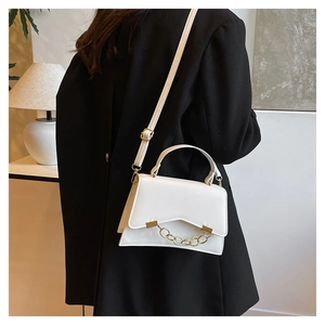 Close-up of a white leather crossbody bag with a gold chain on a black blazer