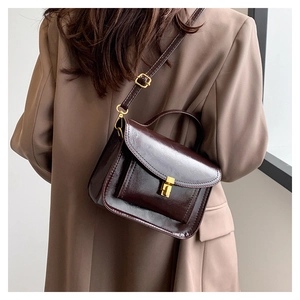 Detail of dark brown glossy wax leather crossbody bag with golden buckle and strap