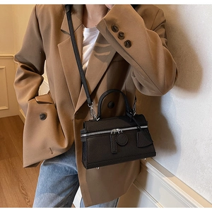 Detail of black pebbled leather box bag with sturdy top handles and detachable shoulder strap