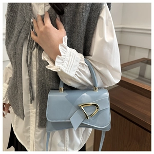 Close-up of light blue handbag featuring a gold geometric buckle and lace-up details