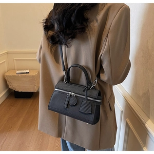 Model wearing a black crossbody box bag with textured finish and dual zipper detail