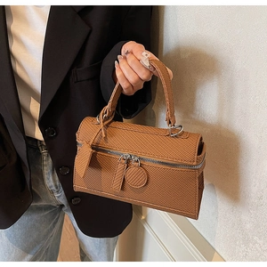 Close-up of tan textured leather handbag with dual metal zippers and reinforced handle