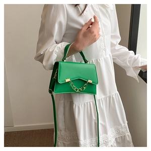 Detail of green leather handbag with decorative metal chain on white lace dress background