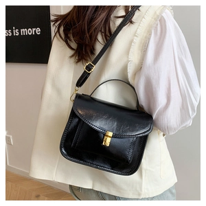 Detail of black glossy wrinkled leather bag with gold square buckle and handle strap