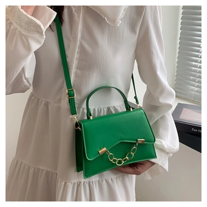 Woman carrying a green leather crossbody bag with decorative gold chain link detail