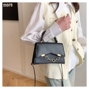 Model showing a structured black handbag with gold chain detail and crossbody strap