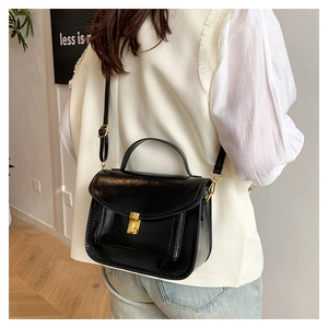 Détail d'un sac messager noir en cuir huilé avec fermoir doré porté par un modèle