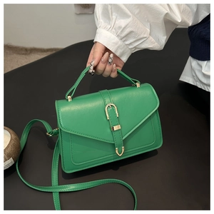 Detail of emerald green PU leather handbag with gold buckle and top handle in hand