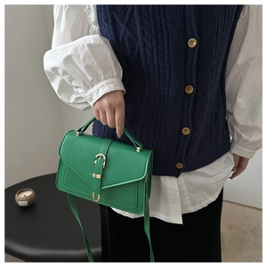 Detail of green leather handbag with envelope flap and gold buckle on a white background
