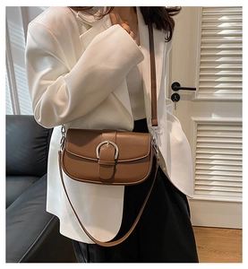Close-up of brown leather saddle bag with silver horseshoe buckle on white blazer
