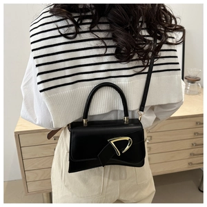 Detailed view of black matte leather bag with golden D-clasp on a striped shawl