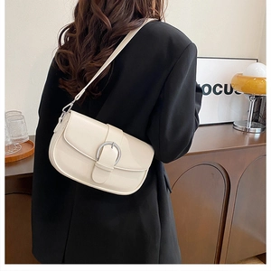 Off-white faux leather saddle bag with silver buckle worn as a shoulder bag in home setting