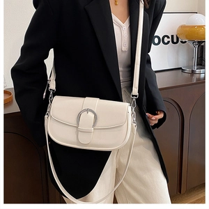 Detailed view of cream saddle bag with large silver buckle and adjustable shoulder strap