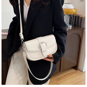 Detail of a beige leather saddle bag with a large silver horseshoe buckle on a model