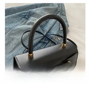 Detailed close-up of the black leather bag featuring a gold horseshoe buckle and top handle