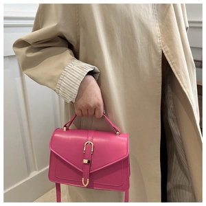 Detail of rose pink crossbody bag with gold buckle on a stylish khaki trench coat