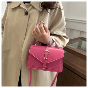 Detail of vibrant magenta crossbody bag featuring a signature gold buckle and top handle