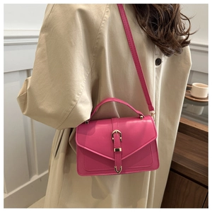 Detail of hot pink envelope crossbody bag with gold U-shaped buckle on a khaki coat