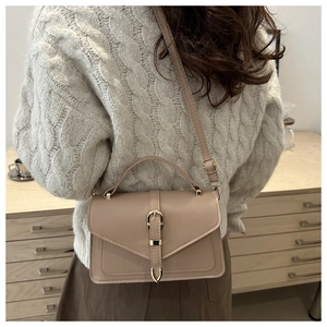 Beige faux leather crossbody bag with gold hardware shown in a lifestyle casual setting