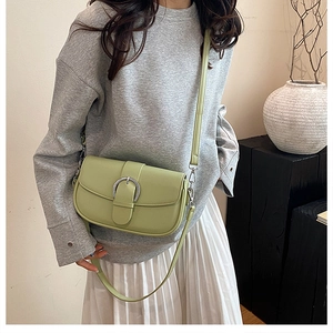 Close-up of light green crossbody saddle bag with horseshoe buckle and leather strap