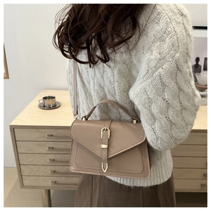 Detail of a minimalist light beige crossbody bag with metal buckle on a cozy knit sweater