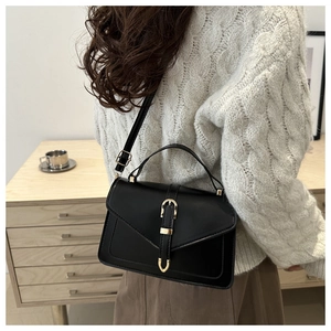 Close-up of black crossbody bag with gold hardware worn over a white knit sweater