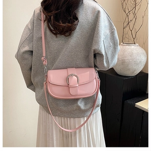 Detail of a minimalist pink leather saddle bag worn by a model in a modern interior