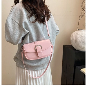 Side view of a woman wearing a pink retro faux leather saddle bag with silver buckle