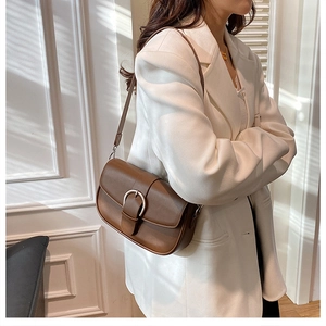 Detail of a brown leather saddle bag with a large metal buckle worn by a model in a white suit
