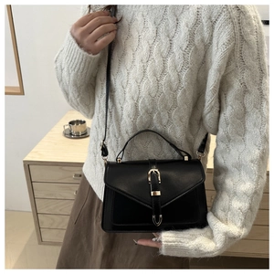 Detail of a black matte leather crossbody square bag with a gold metal buckle on a model
