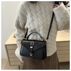 Fashionable black crossbody handbag with gold buckle shown worn with a knit sweater