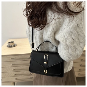 Chic black leather crossbody bag styled with a grey sweater in a minimalist home setting