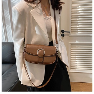 Close-up of a retro brown leather saddle bag with a silver horseshoe buckle on a white suit