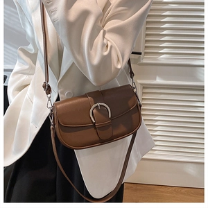 Close-up of vintage brown saddle bag with silver horseshoe buckle on white blazer