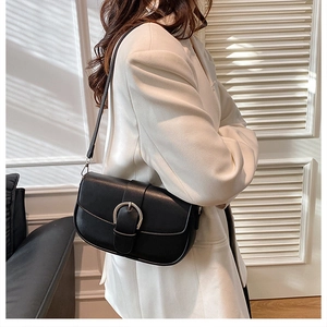 Detail of a black faux leather saddle bag with silver horse-bit buckle on a wool coat
