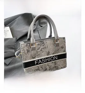 Detailed close-up of the gray floral embroidery and luxury textured fabric on the tote bag