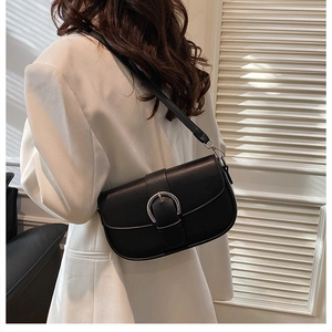 Detail of a black leather saddle bag with silver horseshoe buckle on a white blazer