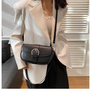 Close-up of black leather saddle bag featuring a round silver buckle on white blazer