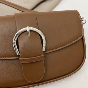 Close-up of brown leather shoulder bag featuring a vintage round silver metal buckle
