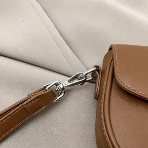 Close-up of premium silver metal hardware and stitching on a brown leather saddle bag