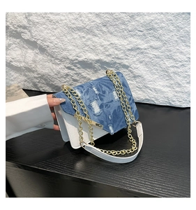 Close-up of distressed denim flap and gold chain detail on a white leather bag