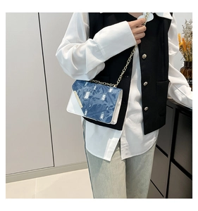 Detail of distressed denim crossbody bag with gold chain and white leather base