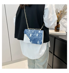 Detail of blue denim and white leather crossbody bag with gold chain strap on a model