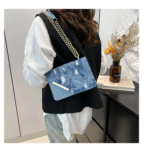 Detail of blue denim shoulder bag with distressed design and gold chain strap on model