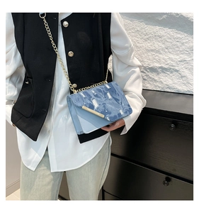 Detail of distressed denim crossbody bag with gold hardware worn by a model
