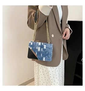 Detail view of denim and black leather crossbody bag with golden chain strap on model